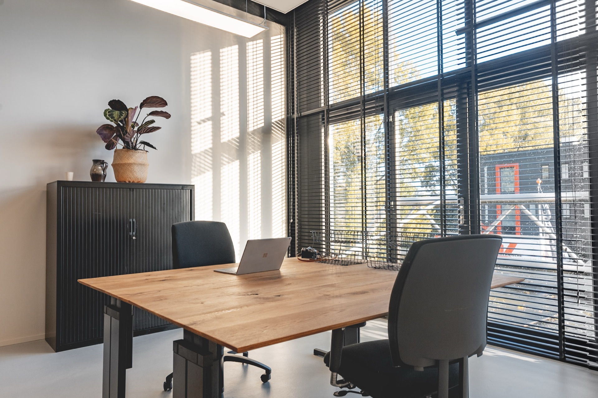Werkplek met eiken bureau en laptop aan het raam in het L-kantoor