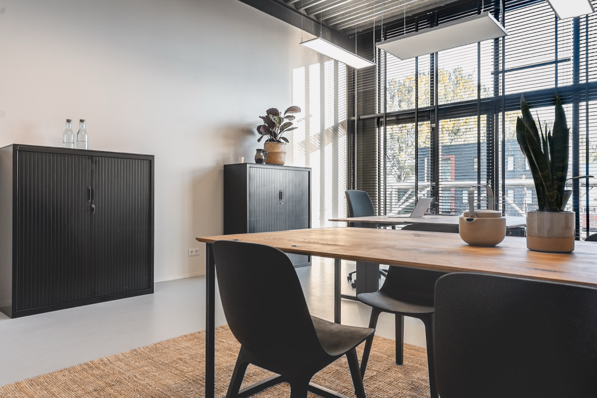 Overlegtafel met stoelen, archiefkasten en planten bij het raam