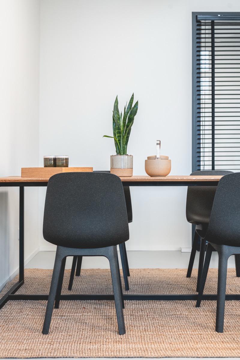 Werktafel met plant en zwarte stoelen op jute vloerkleed